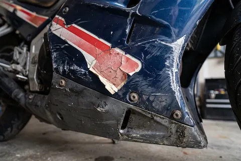 Close-up of a sportbike fairing with tip-over scrapes and a cracked, peeling stripe decal